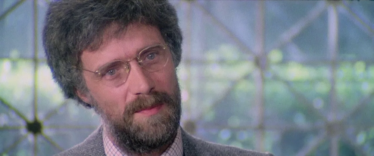 House By The Cemetery (1981) movie still: closeup — The background shows a grid-patterned window with light greenery visible outside the glass. A…