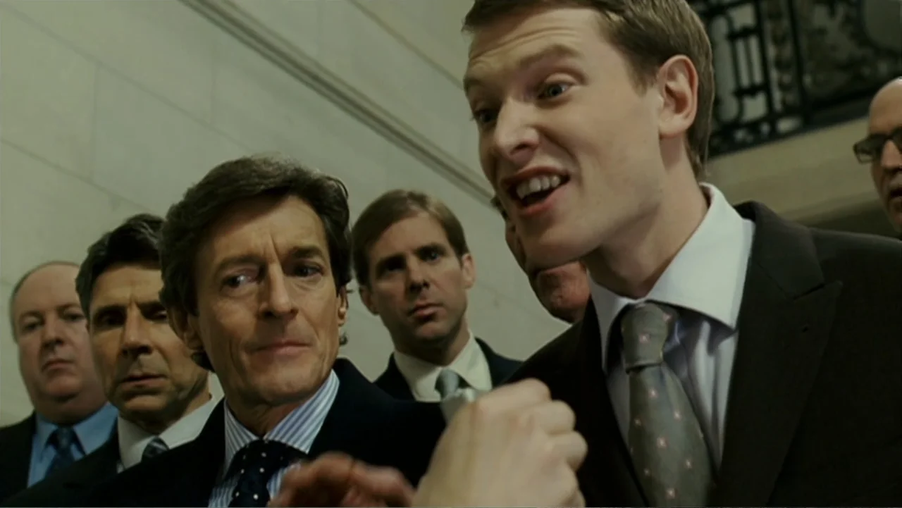 Penelope (2007) movie still: medium — A group of businessmen in suits gather in a bright, modern interior lobby. A younger man addresses the group…