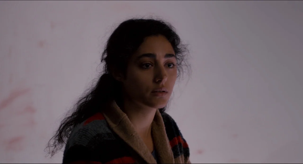 The Night Eats the World (2018) movie still: closeup — A woman stands in a brightly lit, nearly featureless white room. The subject looks off-camera…