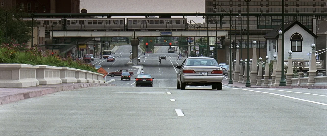 A Family Thing (1996) movie still: wide — An urban road stretches forward under an elevated train track with various cars traveling. A light-colored…
