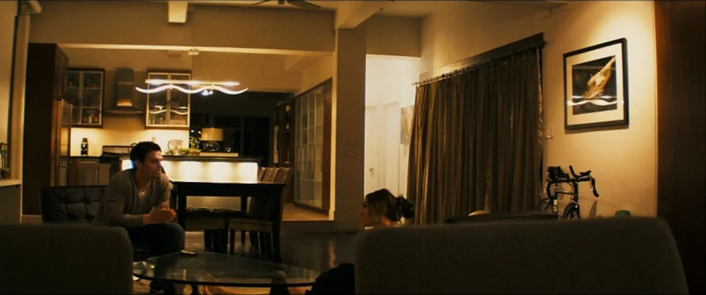 The Girlfriend Experience (2009) movie still: wide — An open plan loft apartment features a modern kitchen and a living area at night. A man sits at…