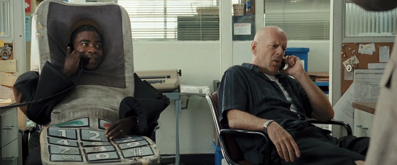 Cop Out (2010) movie still: medium — A cluttered police administrative space features filing cabinets and a bulletin board background. Two men sit…