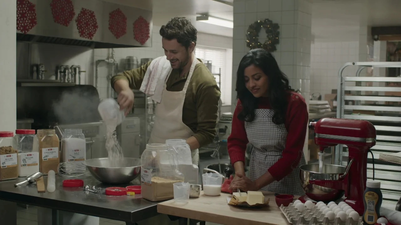 A Gingerbread Christmas (2022) movie still: medium — A professional kitchen features stainless steel surfaces and various baking ingredients. A man…