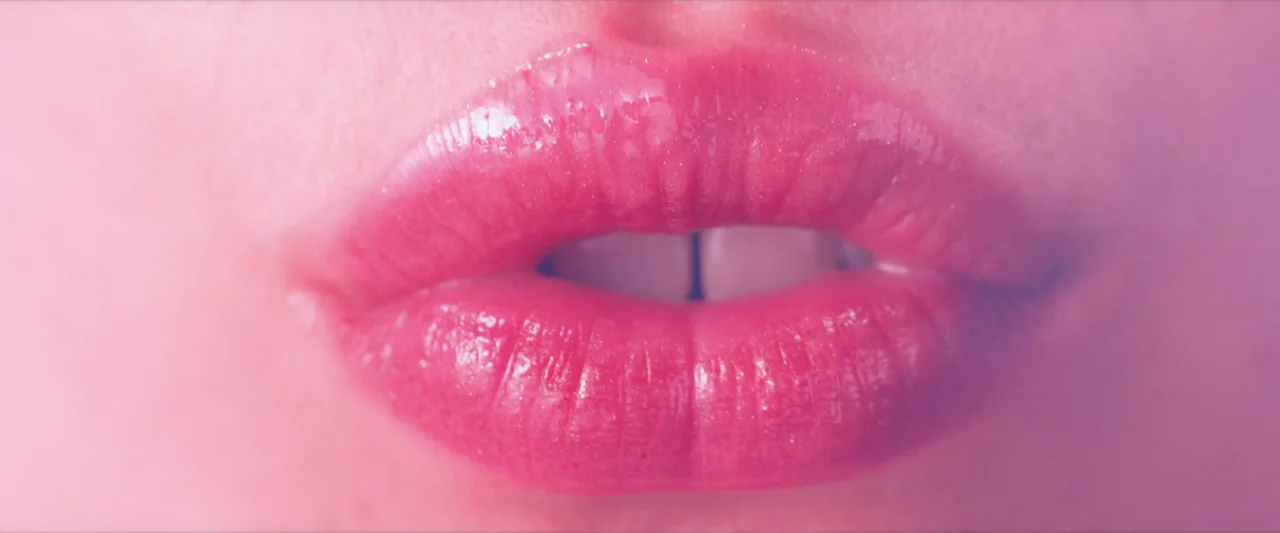 The Substance (2024) movie still: closeup — A close-up frame focuses exclusively on a pair of human lips. The lips are painted with a glossy pink…