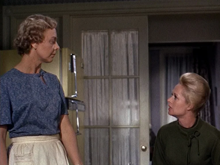 Marnie (1964) movie still: medium — A mid-century home interior features a yellow refrigerator and a glass-paned interior door. Two women stand in…
