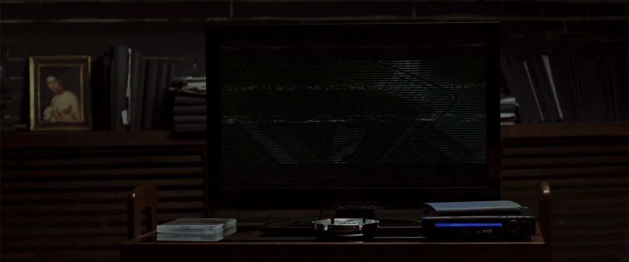 Anna (2013) movie still: medium — A dark room features a television displaying static noise atop a wooden console table. The console holds a media…