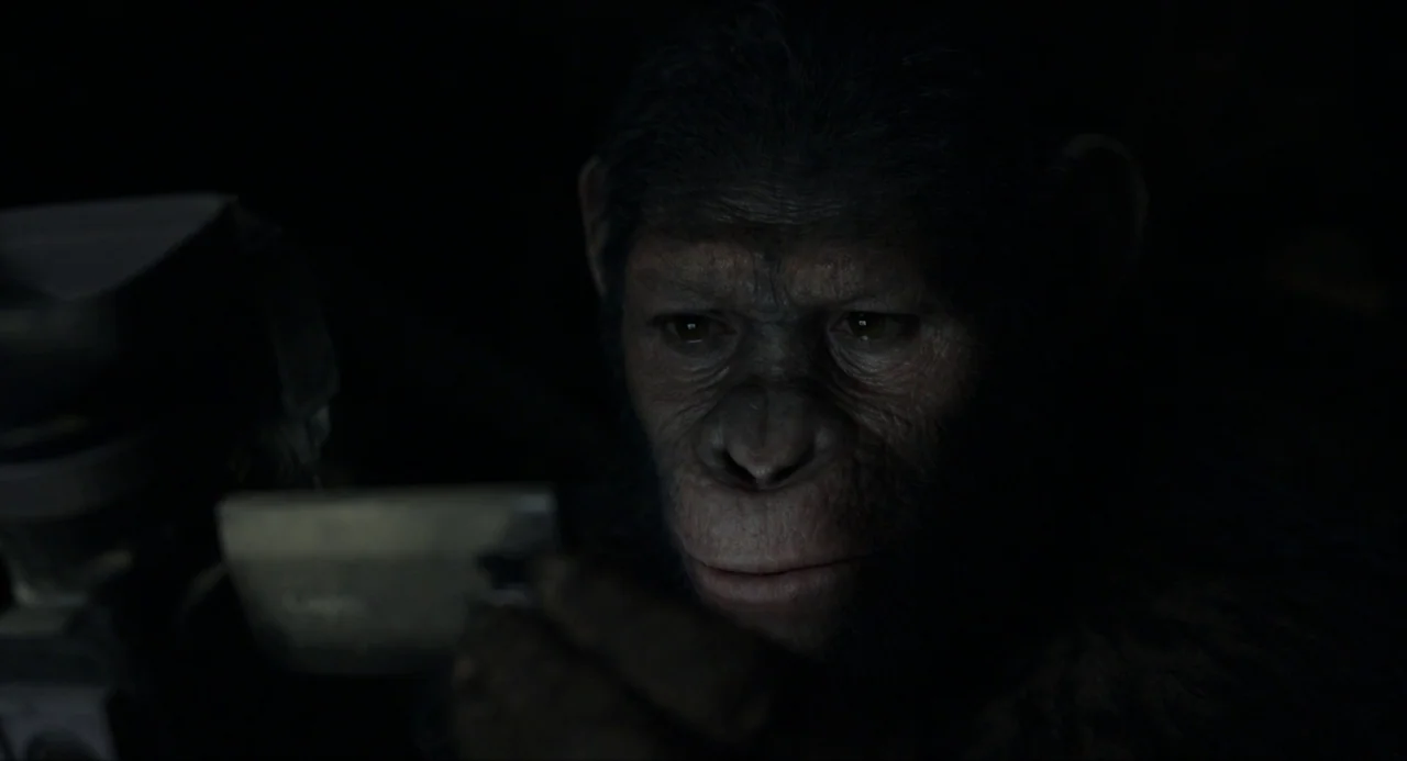 Dawn of the Planet of the Apes (2014) movie still: closeup — A dark space provides a black background for the illuminated face of a chimpanzee. The…