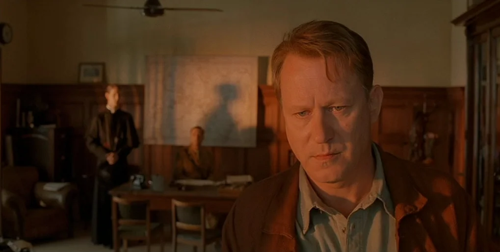 Dominion: Prequel to the Exorcist (2005) movie still: medium — A wood-paneled office contains a desk with two other men stationed in the background.…