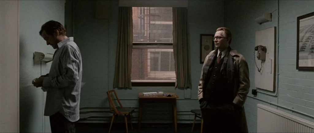 Tinker Tailor Soldier Spy (2011) movie still: medium — A sparse interior with light teal painted brick walls and a single central window. Two men…