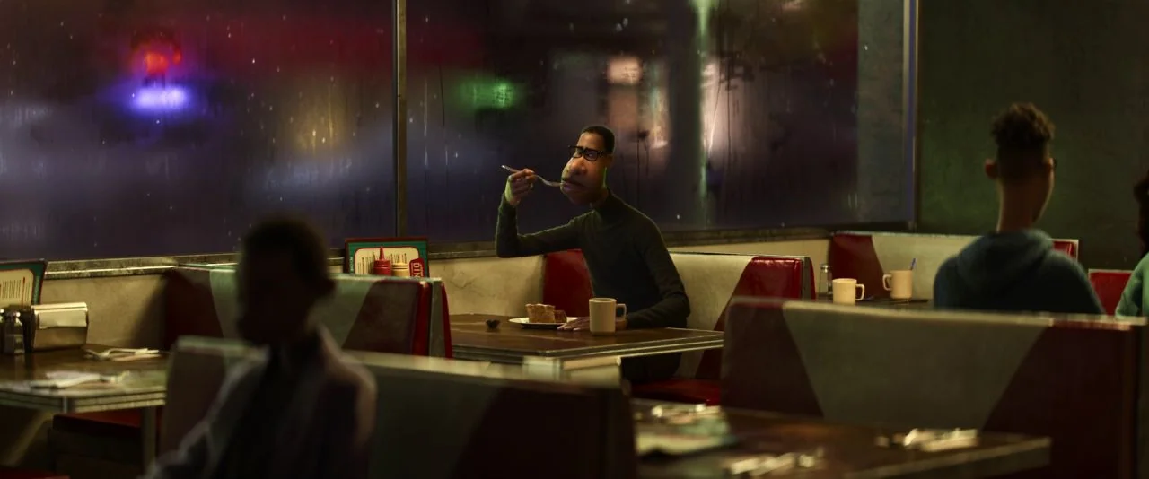 Soul (2020) movie still: medium — A dimly lit diner at night with vinyl booths and tables near a window. A man in a green sweater eats a piece of…