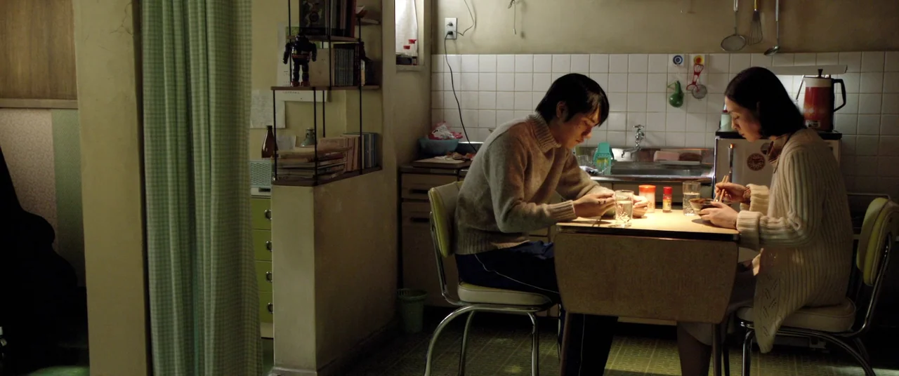 Norwegian Wood (2010) movie still: medium — A small residential kitchen features a white-tiled wall with assorted cooking utensils hanging above. A…