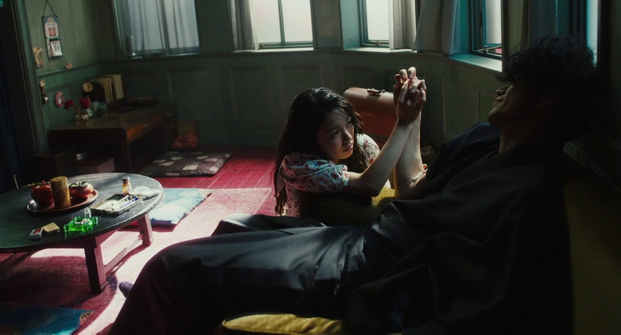 No Longer Human (2019) movie still: medium — An interior living space features green paneled walls, a small low table, and window light. A woman in…