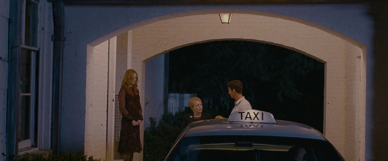 Stoker (2013) movie still: wide — A white brick portico with an archway connects to a house at night. A taxi is parked under the structure while…