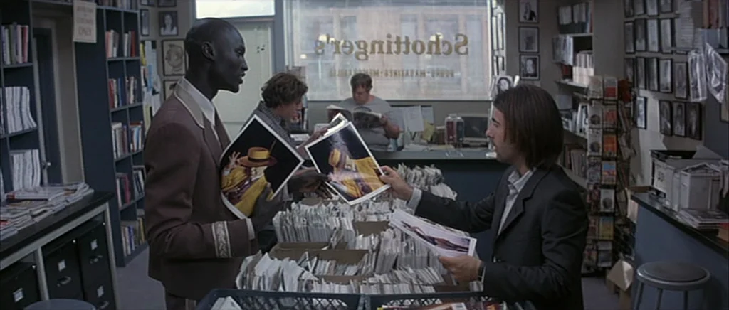 I Heart Huckabees (2004) movie still: medium — A cluttered shop interior features rows of shelves filled with magazines and framed photographs. Two…