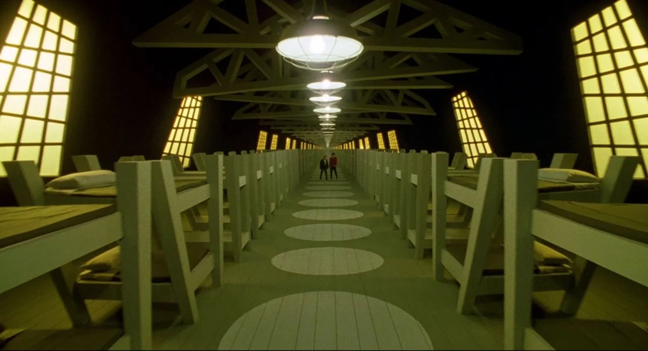 Bill and Ted’s Bogus Journey (1991) movie still: wide — A symmetrical long dormitory space features rows of identical wooden bed frames on both…