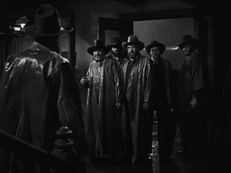 My Darling Clementine (1946) movie still: medium — A dark tavern entrance lit by a single overhead light shows heavy rain falling outside. Four men…