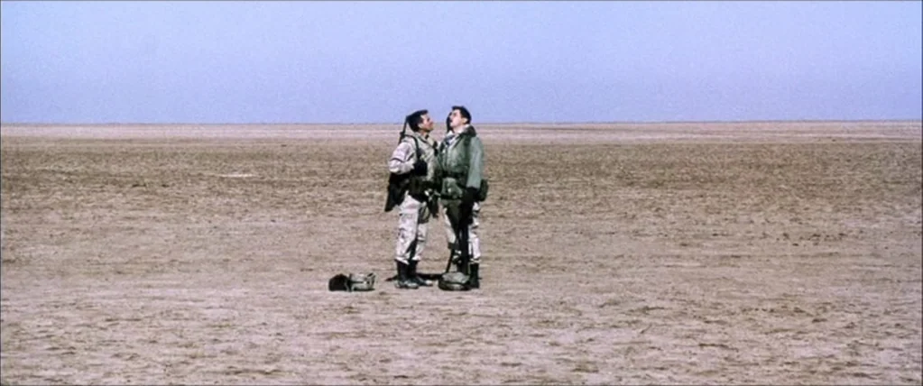 Three Kings (1999) movie still: wide — A vast, empty desert landscape extends to the horizon under a clear blue sky. Two soldiers in camouflage…