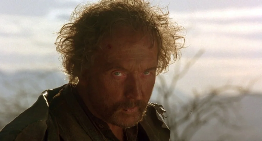 The Quick and the Dead (1995) movie still: closeup — A man stands in an arid desert environment under a bright, overcast sky. The subject looks…