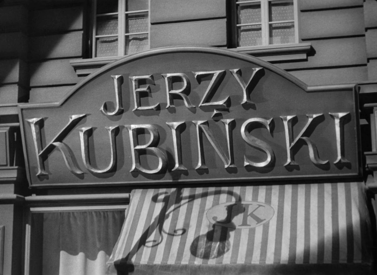 To Be or Not To Be (1942) movie still: closeup — A storefront with an arched sign reading Jerzy Kubinski hangs above a striped awning. The facade…