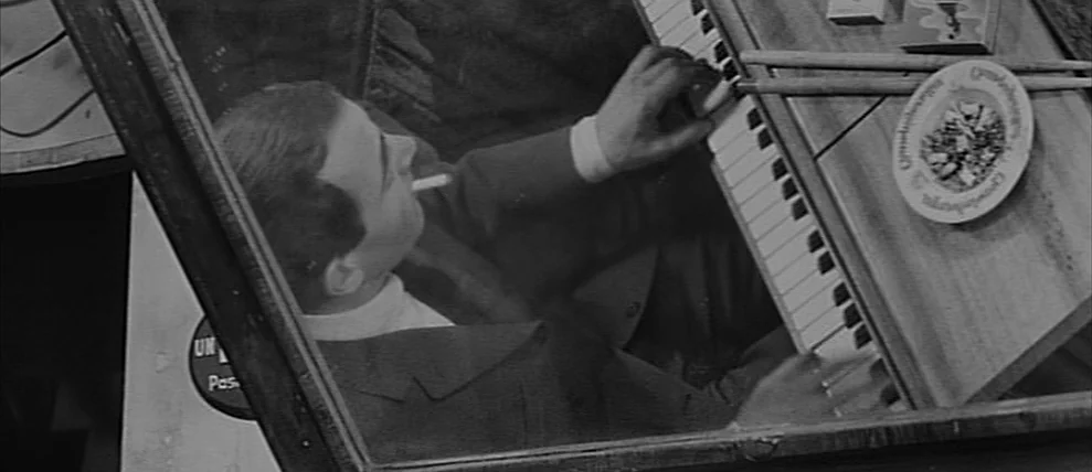 Shoot The Piano Player (Tirez Sur Le Pianiste) (1960) movie still: medium — A man sits at a piano in a dimly lit bar setting. He plays the keys…