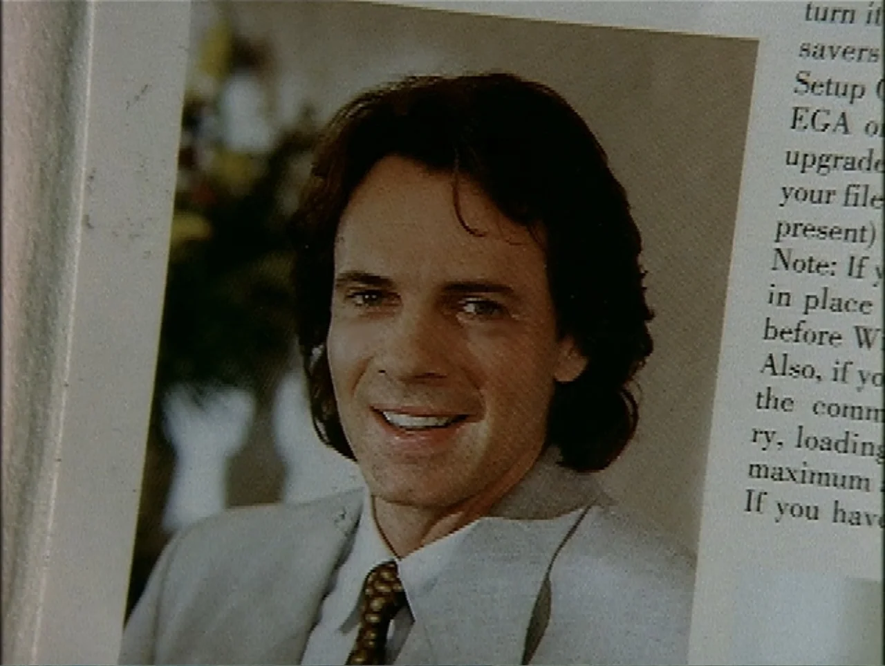 A Change of Place (1994) movie still: closeup — A close-up photograph of a man printed on a textured white paper surface. The man wears a…