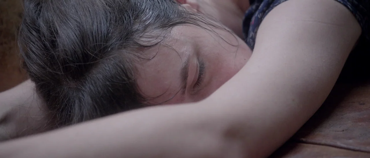 Nymphomaniac Vol 2 (2013) movie still: closeup — A person rests with their head on a wooden surface. Their dark hair is damp and their arms are…