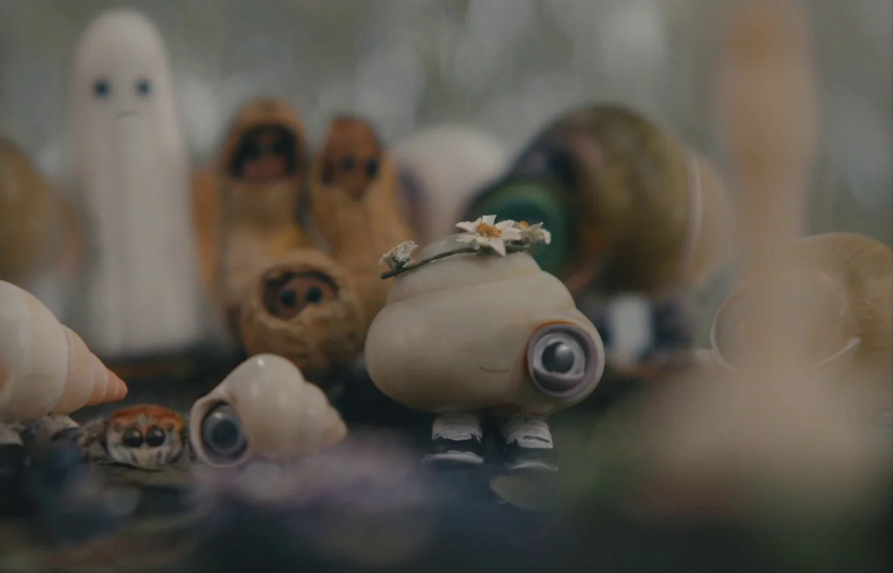 Marcel the Shell with Shoes On (2021) movie still: closeup — A collection of small figurines rests on a flat, out-of-focus surface. A shell-bodied…