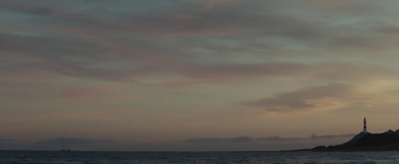 The Light Between Oceans (2016) movie still: establishing — A vast expanse of ocean meets a cloudy, muted-toned sky at twilight. A small lighthouse…