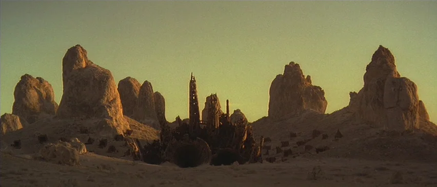 Planet of the Apes (2001) movie still: establishing — A vast desert landscape features towering natural rock formations and a central metallic…