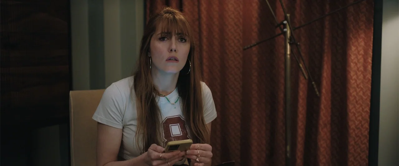 Play Dirty (2025) movie still: medium — A recording booth features a metallic microphone stand and heavy red patterned fabric curtains. A young…