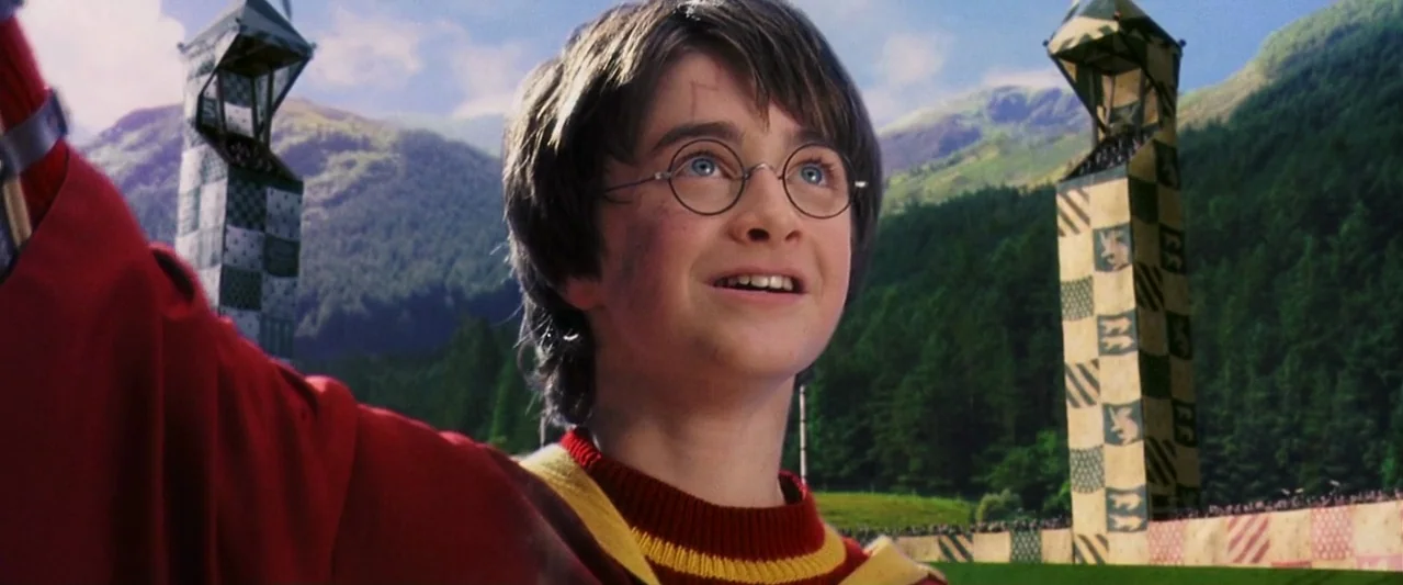 Harry Potter and the Philosopher's Stone (2001) movie still: closeup — A vast outdoor athletic field features two tall checkered towers and distant…