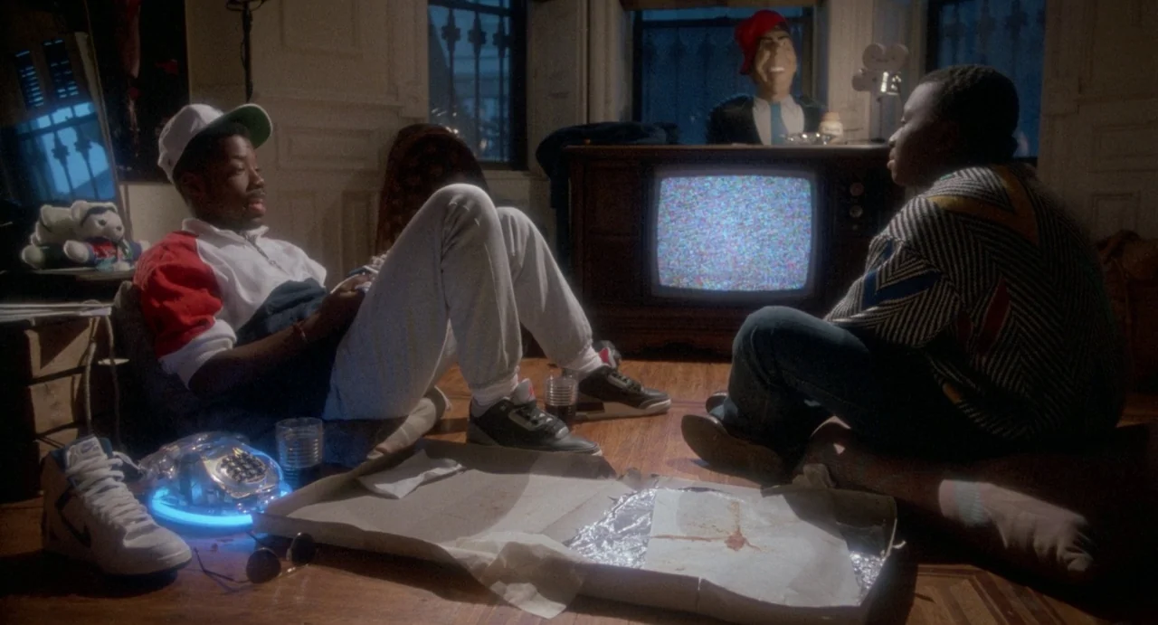 Def By Temptation (1990) movie still: medium — A 1990s living room features hardwood floors, a vintage television with static, and an open pizza…
