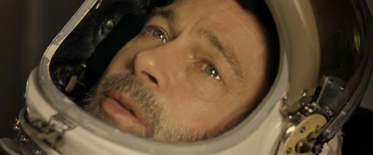 Ad Astra (2019) movie still: closeup — A close-up of an astronaut wearing a white helmet inside a spacecraft cockpit. The man stares upward with a…