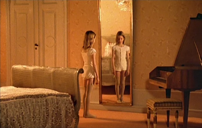 Autumn Sonata (1978) movie still: fullbody — A room with patterned wallpaper contains an upholstered bed and a grand piano. A young girl in white…