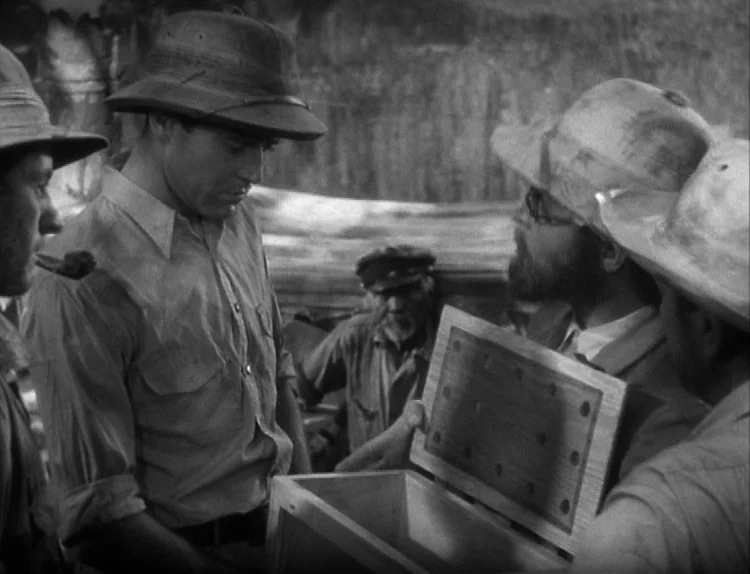 The Lady Eve (1941) movie still: medium — A dimly lit interior space with wooden walls houses several men in safari attire. The men gather around an…