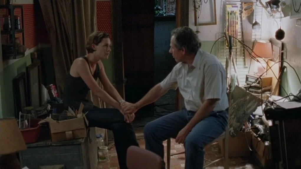 Junebug (2005) movie still: medium — A cluttered workshop space filled with various hand tools and miscellaneous boxes and supplies. A woman sits on…