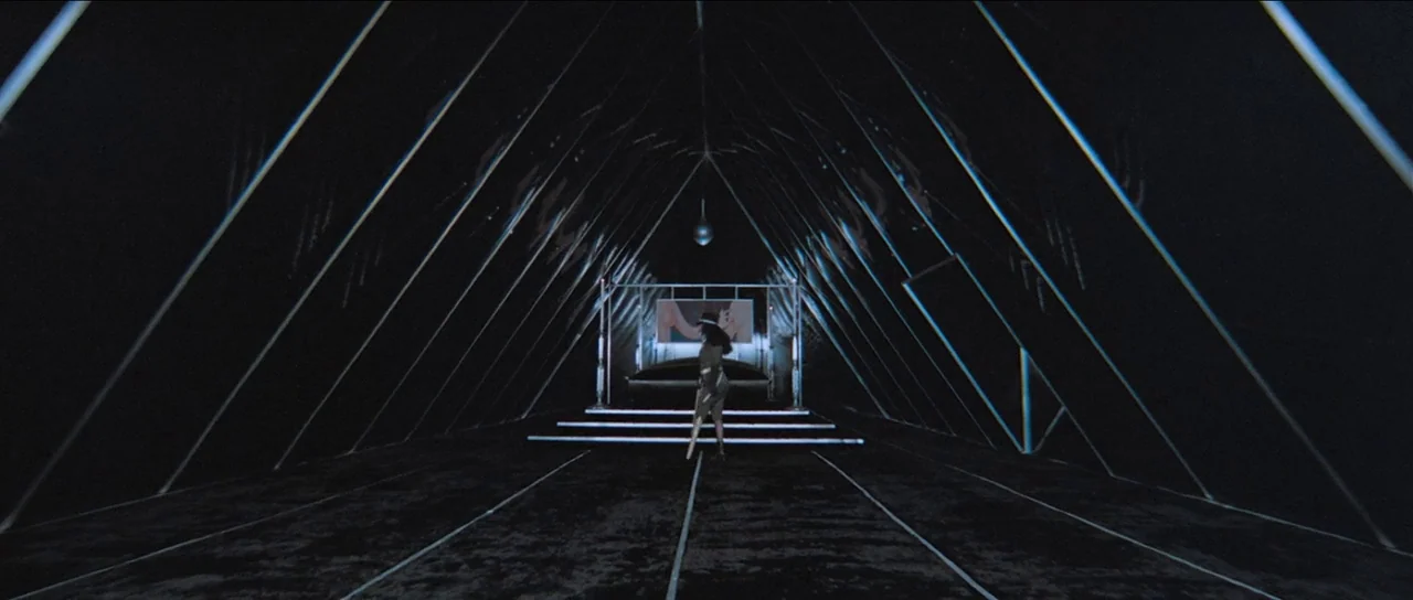 The Holy Mountain (1973) movie still: wide — A dark, triangular stage structure features sharp geometric light lines along its interior walls. A…