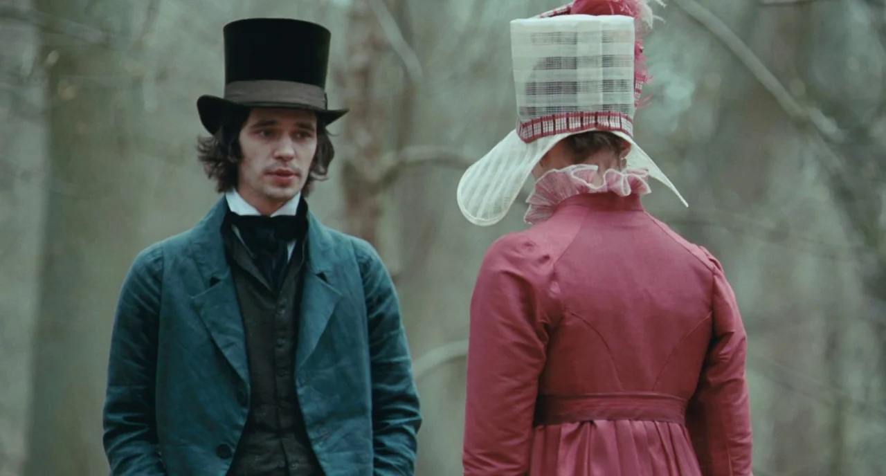 Bright Star (2009) movie still: medium — A man and a woman stand within a bare, overcast woodland area in period dress. The man looks at the woman…