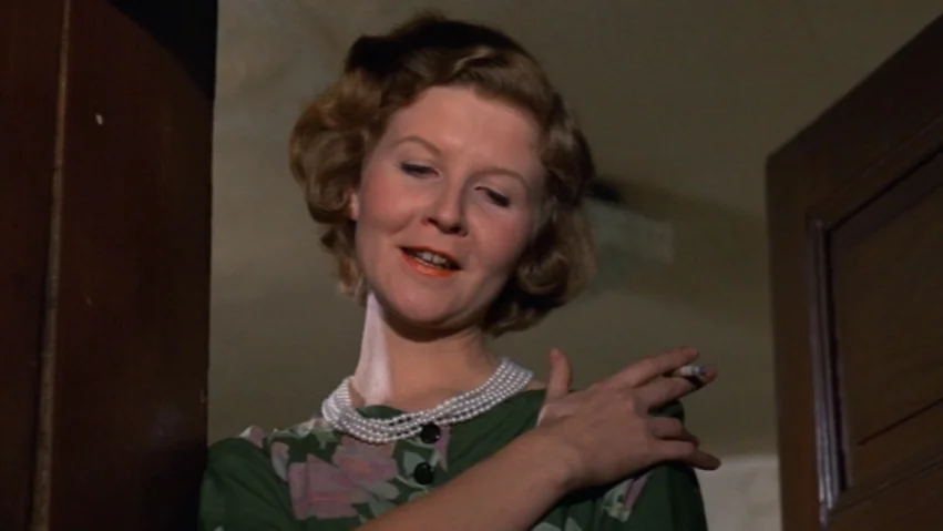 Tenderness of the Wolves (1973) movie still: closeup — A woman stands in a narrow doorway framed by dark wood panels. She wears a floral blouse and…