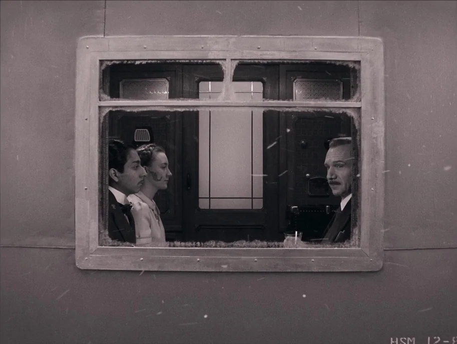 The Grand Budapest Hotel (2014) movie still: medium — A vintage 1930s train compartment features wood-paneled walls and a rectangular observation…