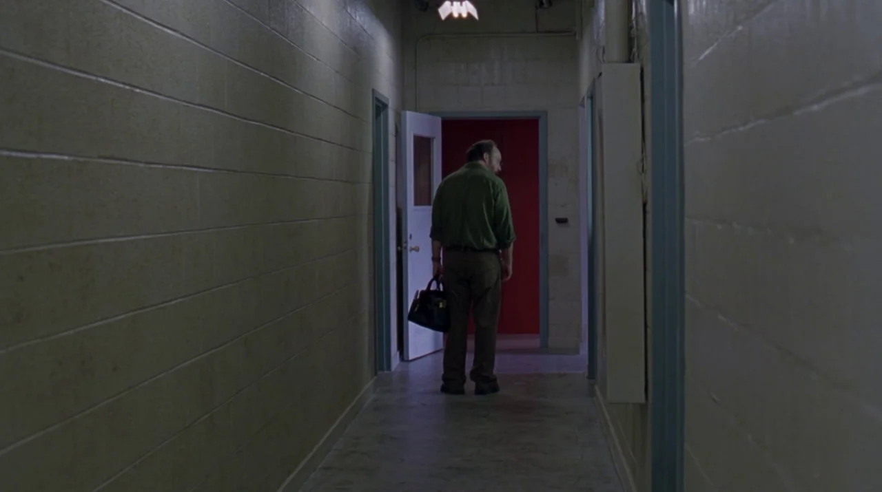 Lady in the Water (2006) movie still: fullbody — A narrow corridor features painted concrete block walls and light grey linoleum flooring. A man…
