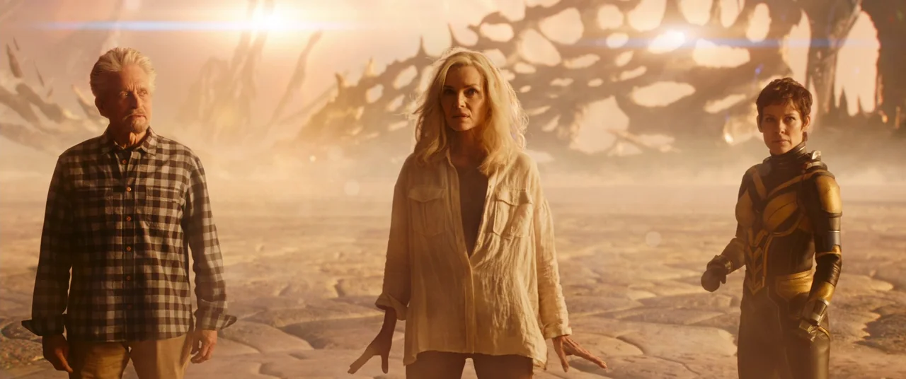 Ant-Man and the Wasp: Quantumania (2023) movie still: fullbody — An alien landscape features a cracked dry surface under a hazy golden sky. Three…