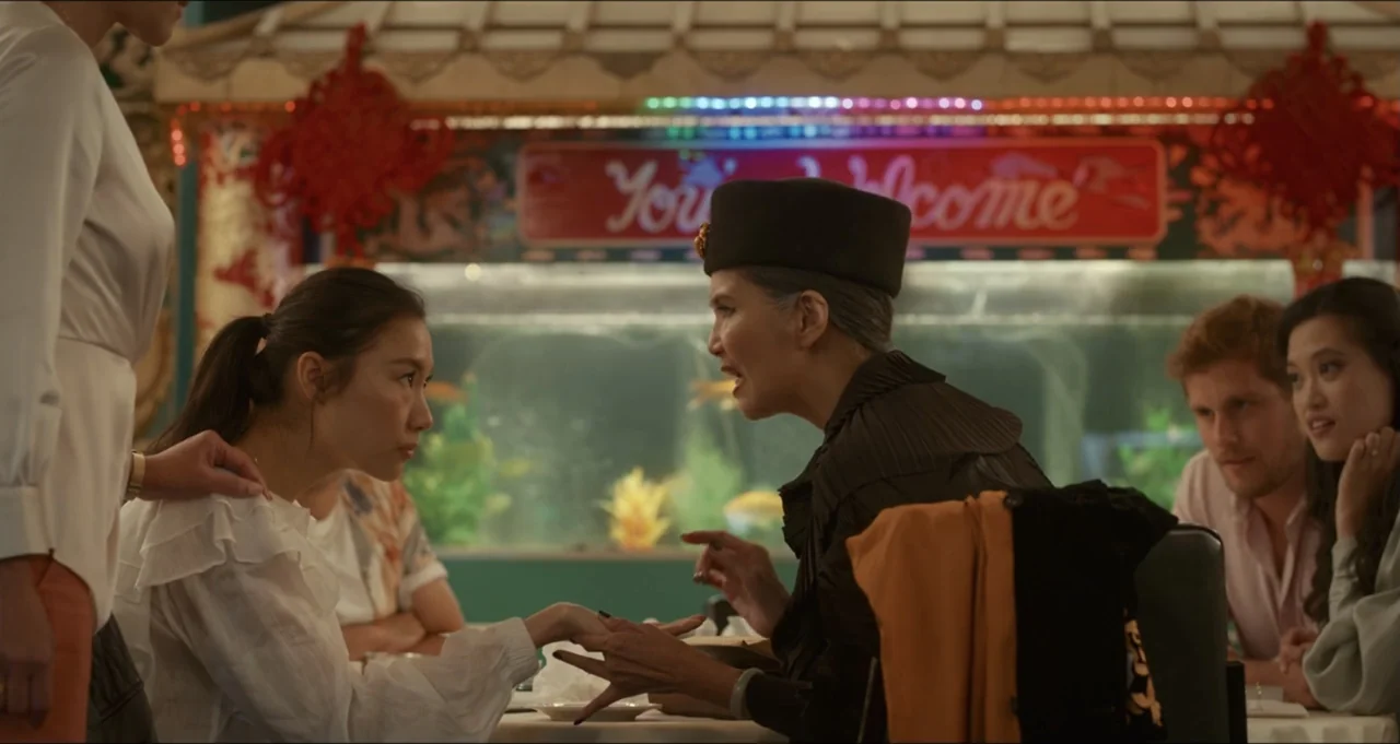 Five Blind Dates (2024) movie still: medium — An interior restaurant table with a large aquarium visible in the background. Two women face each…