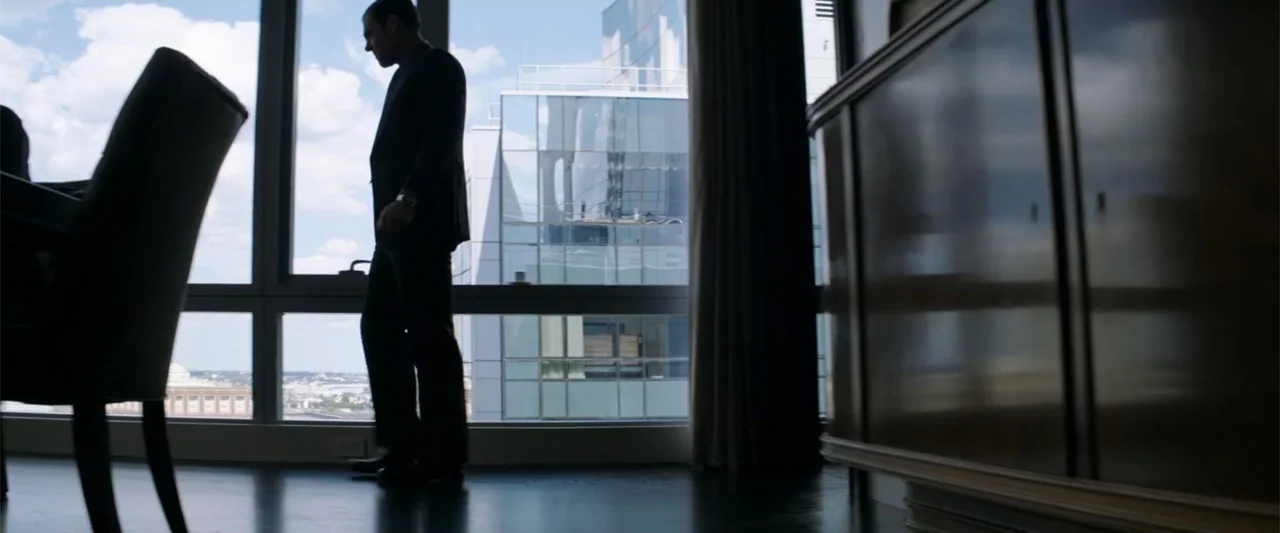 The Equalizer (2014) movie still: fullbody — A modern high-rise room features large floor-to-ceiling windows looking out over a city. A man in a…