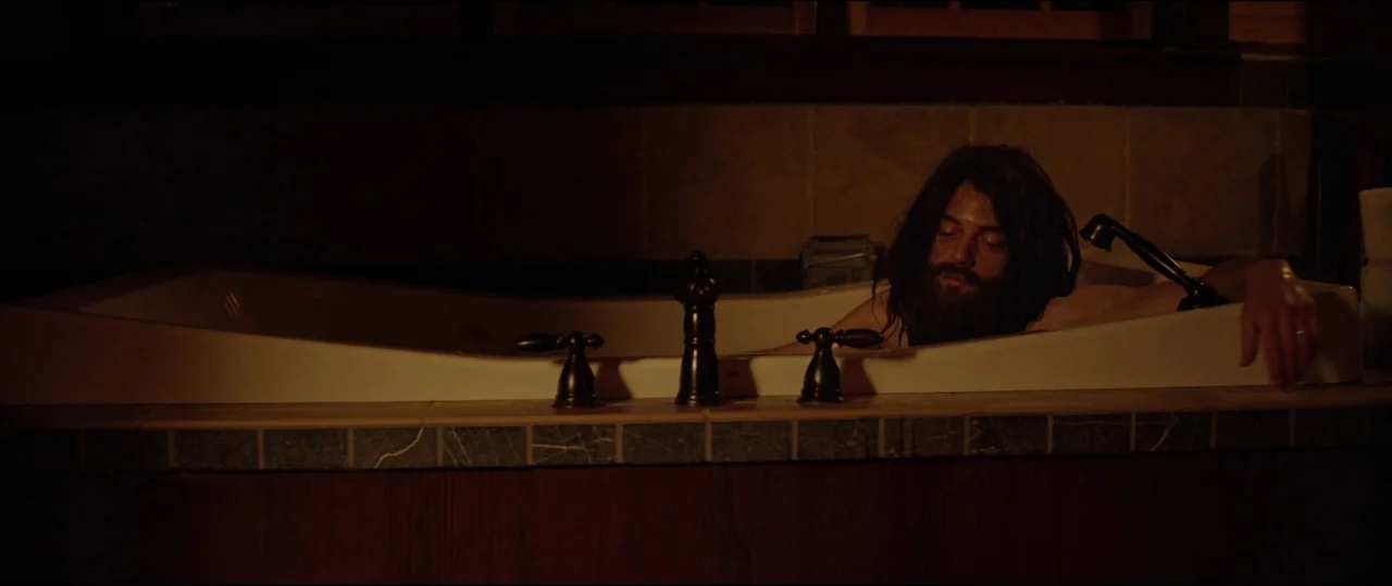 Buster’s Mal Heart (2016) movie still: medium — A dark bathroom interior features a large white jetted bathtub tiled with dark stone. A man with a…