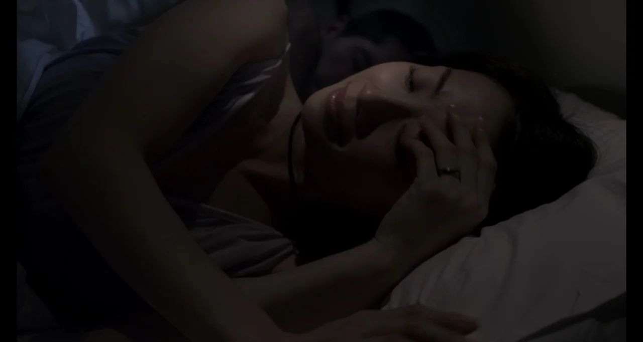 Ninja: Shadow of a Tear (2013) movie still: closeup — A dark bedroom with two people lying in a bed under white linens. The foreground woman has her…