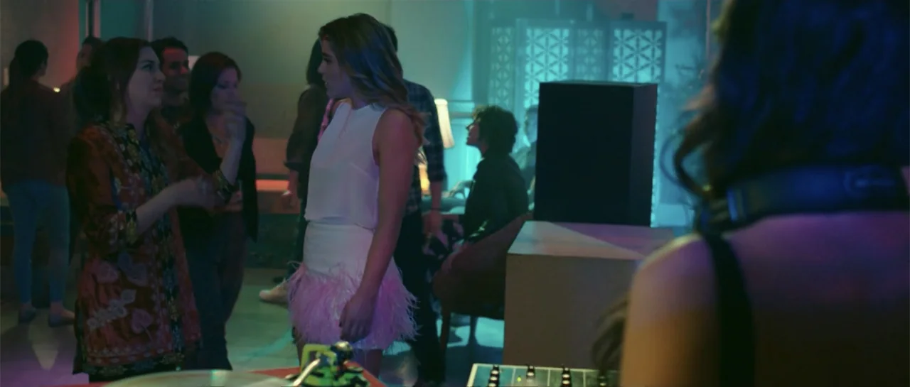 Cindy La Regia (2020) movie still: medium — A dimly lit club interior features colorful neon accents and various patrons socializing. Two young…