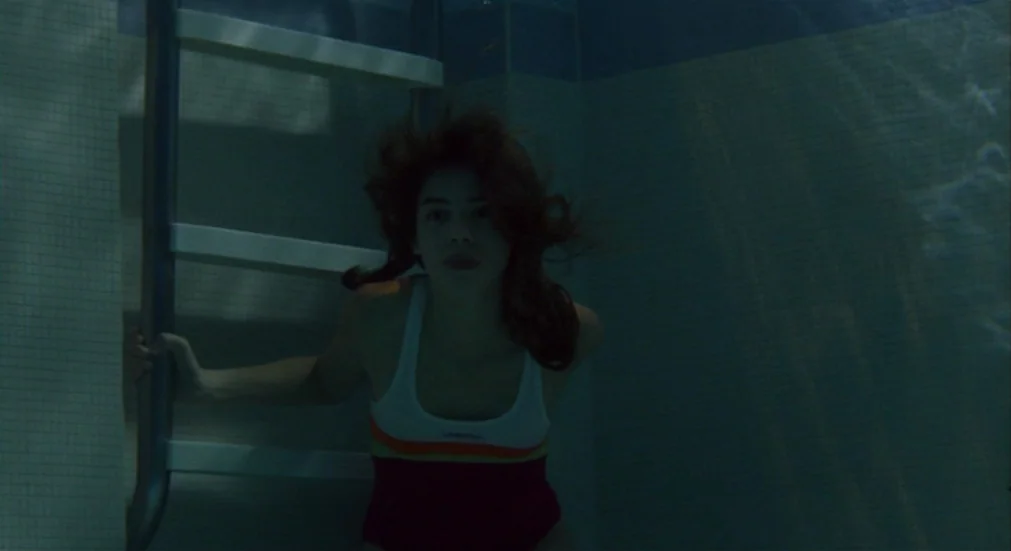 Water Lillies (2007) movie still: medium — A woman is underwater in a tile-walled pool holding onto a metal ladder. She looks directly at the camera…