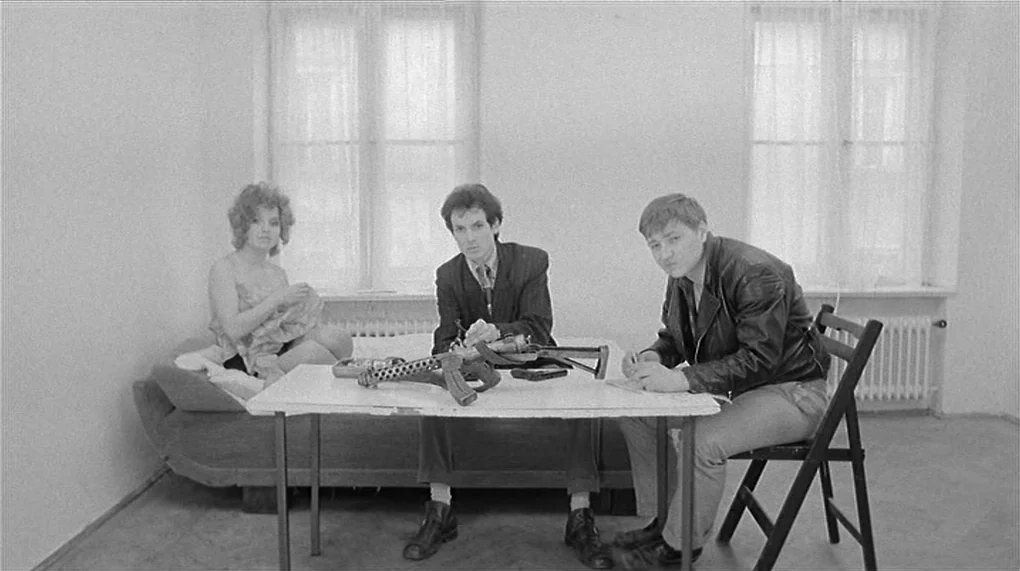 Love Is Colder Than Death (1969) movie still: wide — A sparsely furnished room with two windows and white walls serves as the backdrop. Three people…