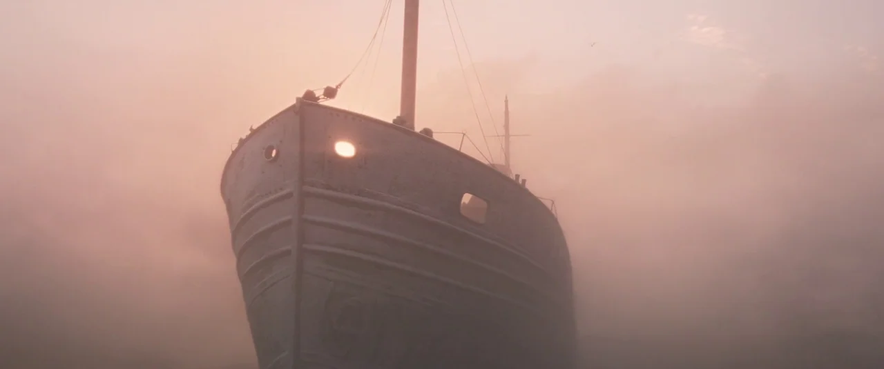 Wonka (2023) movie still: wide — A metal hulled ship moves through a dense fog bank at sunrise. The vessel is partially obscured by the thick, hazy…